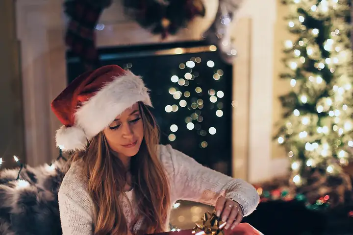 Een lachende vrouw met kerstmuts pakt een cadeau uit bij de boom