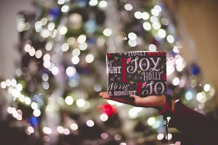 A Christmas gift held up in front of a glowing tree